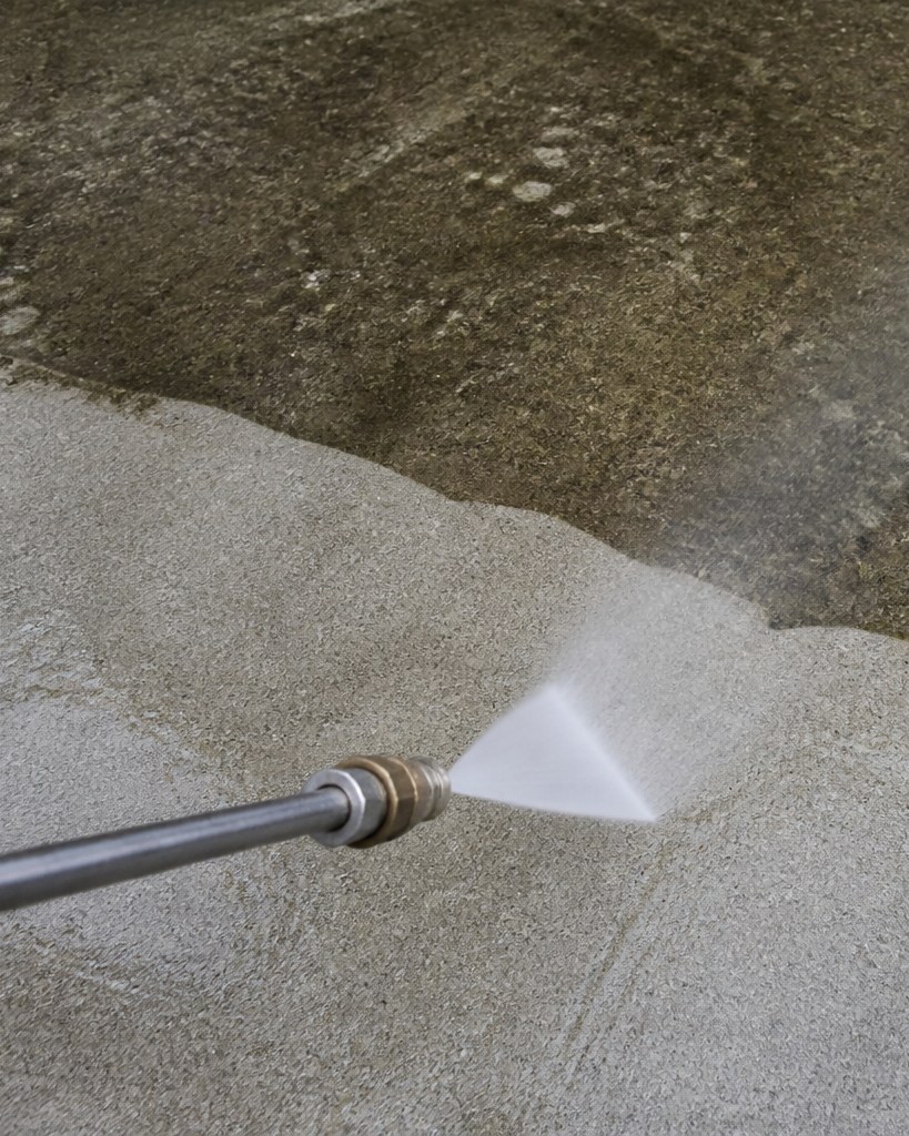 Pressure washer cutting a clean stripe through stained concrete.